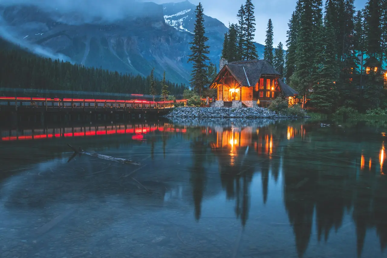 A lit lodge building and footbridge on Emerald Lake, BC, at blue hour, with mountains behind